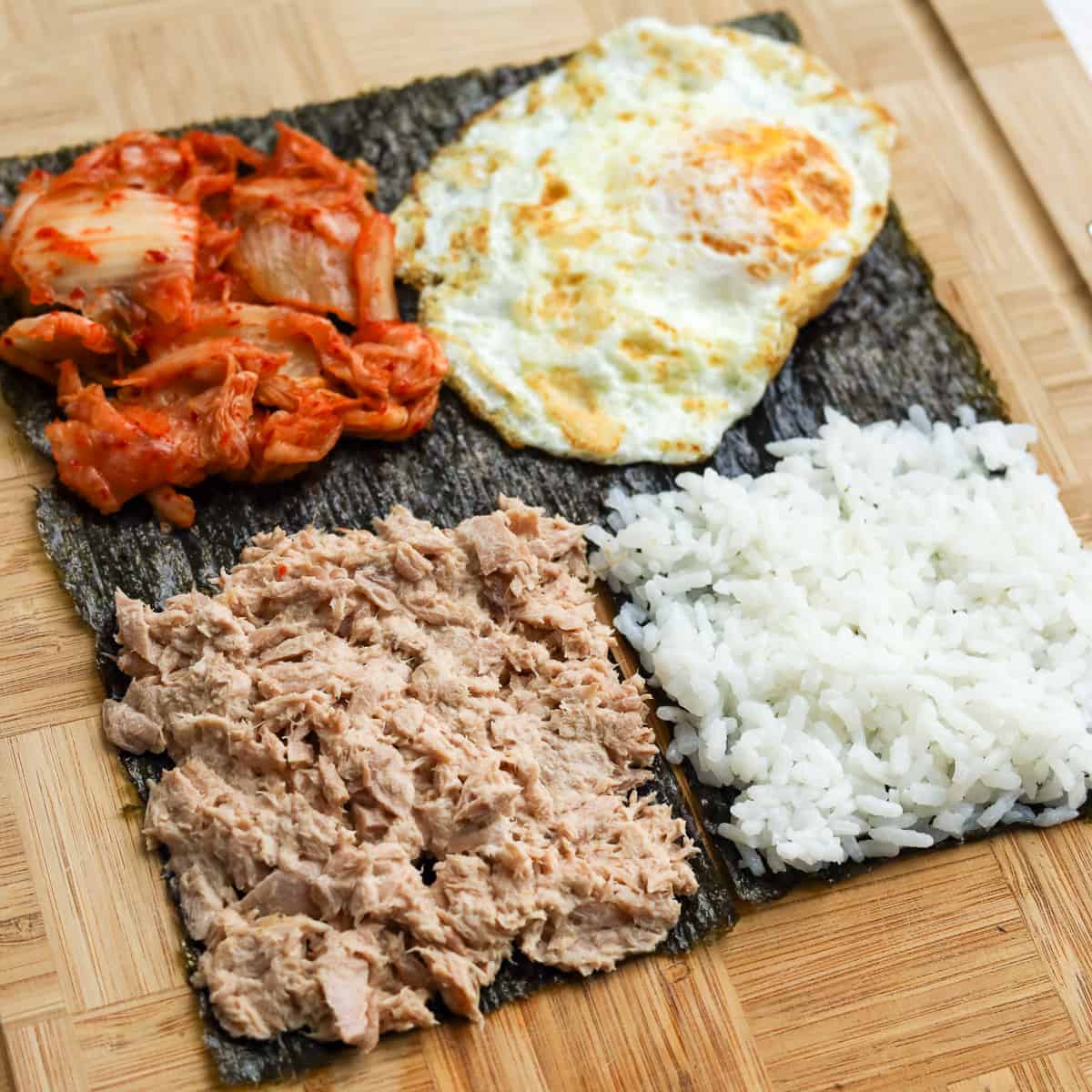 Evenly spread the tuna mayo mixture in the bottom left quadrant. Place the fried egg in the top right quadrant. Spread kimchi in the top left quadrant. Lastly, evenly spread hot cooked rice in the bottom right quadrant. 
