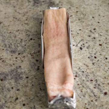 Then place pork belly strips onto a large rectangular sheet of aluminum foil. Wrap the foil around the pork belly strip creating a rectangular box with low walls, so the skin is fully exposed. Do not create tall walls or it will block the heat from crisping the skin. Transfer the wrapped pork to a small baking sheet.