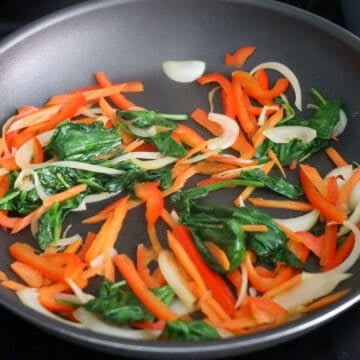 Onions, carrots, bell peppers, and spinach stir-frying in a pan.