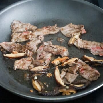 Thinly sliced beef and shiitake mushrooms cooking in a pan.