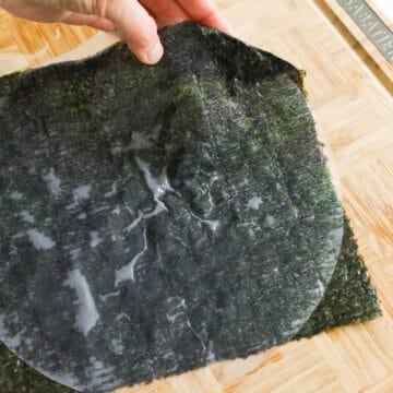 Then quickly place it over the roasted seaweed sheet. Press down on rice paper until it sticks to seaweed. Fold in any empty seaweed corners onto the rice paper. Transfer to a wire rack for this to dry as you work on the other pieces. 