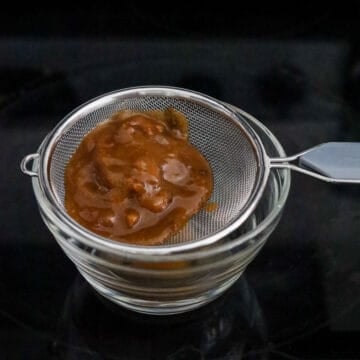 Run the paste through a fine sieve to remove any pulp or seeds. Scrape the back of the sieve. This is tamarind paste. Set aside.