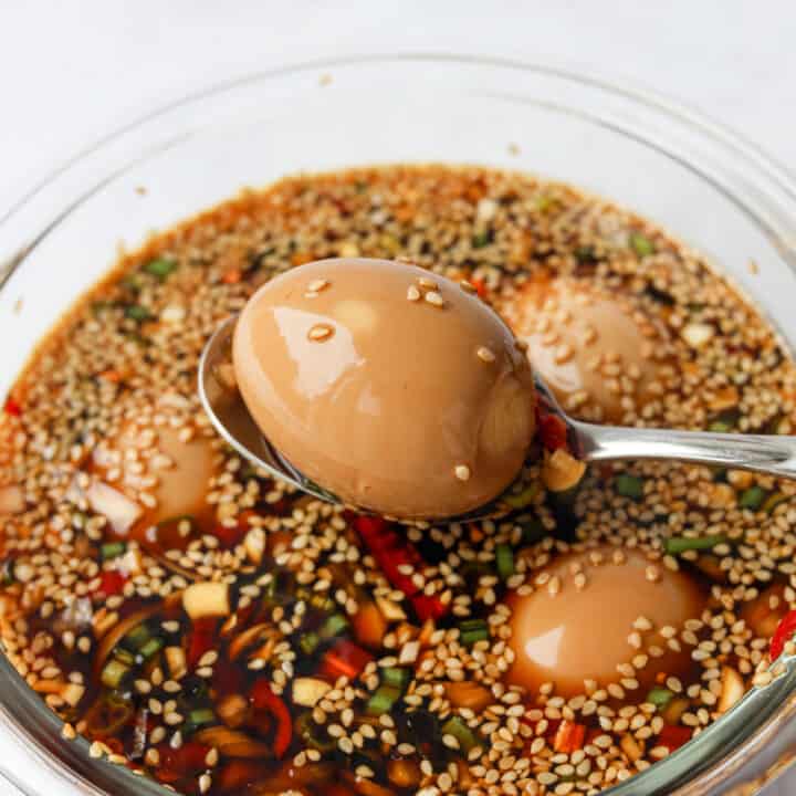 Six brown soy-marinated eggs submerged in liquid inside a container with a paper towel resting on top.