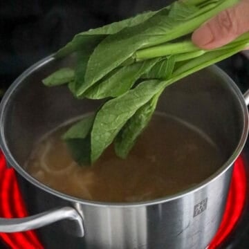 Reduce heat to medium. Blanch greens in boiling hot broth for 1 minute or until vibrant green. Remove greens and transfer to serving bowl on top of noodles.