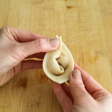 Then bring the two pointed ends of the wings together and pinch to seal them.  Repeat this process for remaining wontons. 