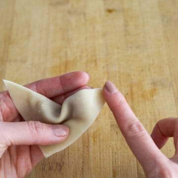 Fold the wonton into a triangle so the opposite corner is sealed to the other one. Push out any air bubbles and seal the edges of the wrapper. With your triangle, lightly dab water on the end of one wing. 