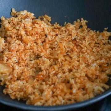 Add in day-old cooked rice, kimchi juice, gochujang, sesame oil and toss everything together until rice are colored red. 