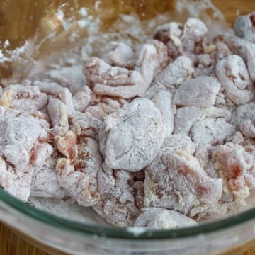Transfer pieces of chicken into a large bowl, followed by cornstarch. Mix to coat each piece evenly with tongs.