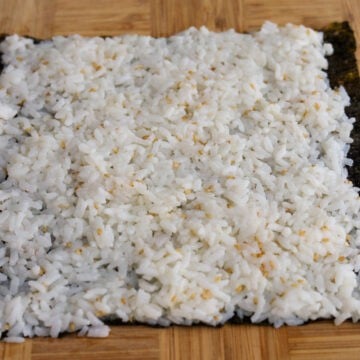 Vertically place a sheet of gim or nori rough side up and shiny side down on a cutting board (or on a bamboo sushi mat if you have one). Place 1 cup or a half portion the seasoned rice into the center of the gim or nori. Using clean hands or a rice paddle, evenly spread the portion of rice out and create a 1-inch border at the end furthest away from you.
