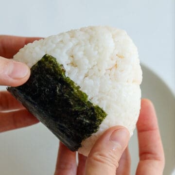 Then remove a sheet of nori from its packaging. Vertically fold the sheet into half and cut at the fold line. Then fold one half into half again and fold again. Cut into 4 vertical strips at the fold line. (Alternatively, you can also use half a sheet of nori per rice ball if you prefer more seaweed!)