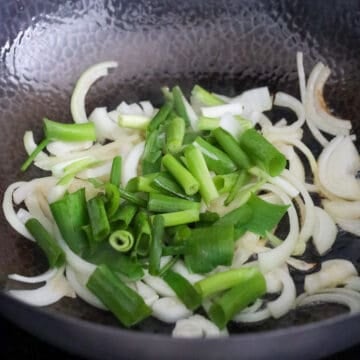 Heat vegetable oil in the same pan on medium-high heat. Sauté yellow onions and cook until translucent. Reduce to medium heat and stir fry green onions with the onions. 