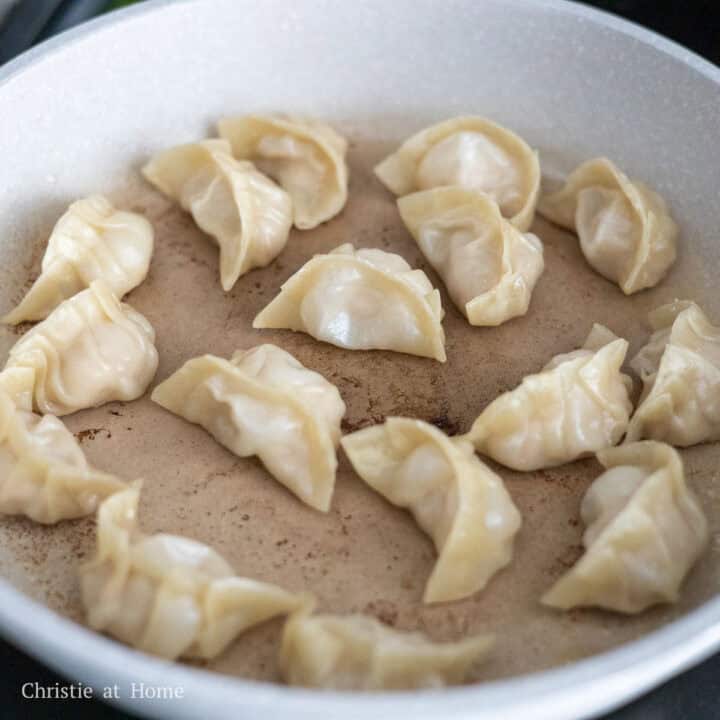 Pan-fried pork and shrimp dumplings with golden brown bottoms sizzling in a pan.