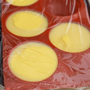 Mango mixture being poured into greased bowls or silicone molds, with air bubbles tapped out and surface smoothed.