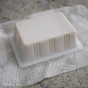 Uncooked block of white silken tofu resting on a white paper towel.