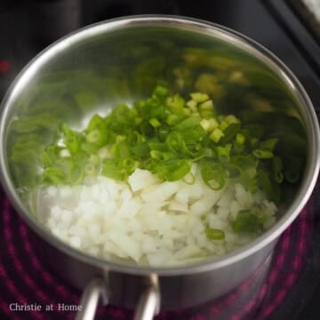 Diced onions, green scallions, and minced garlic sizzling together in oil.