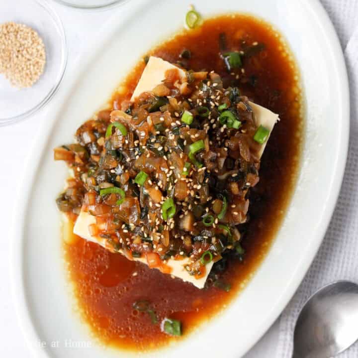 Chilled white silken tofu block topped with dark savory onion sauce, green scallions, and white sesame seeds.