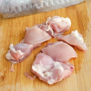 Chicken thighs diced into 1.5-inch pieces on a cutting board.