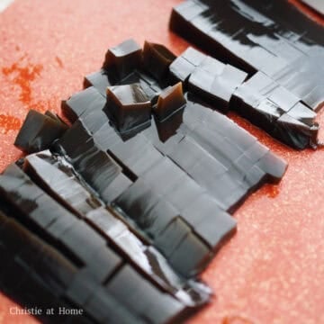 Black grass jelly sliced into small and medium cubes on a flat cutting board.