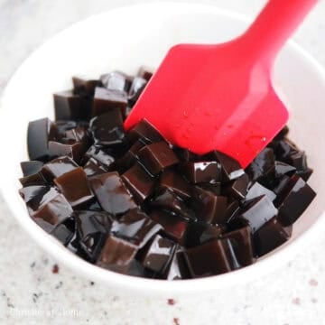 Glistening black grass jelly cubes coated in glossy brown sugar syrup.