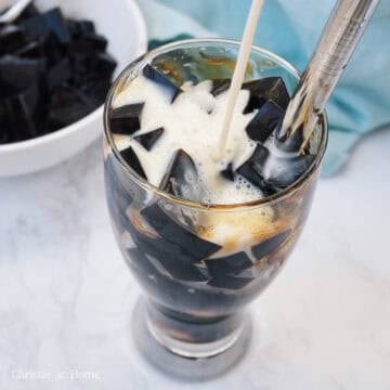 Creamy white milk poured over dark grass jelly cubes, ice, and streaked brown sugar syrup.