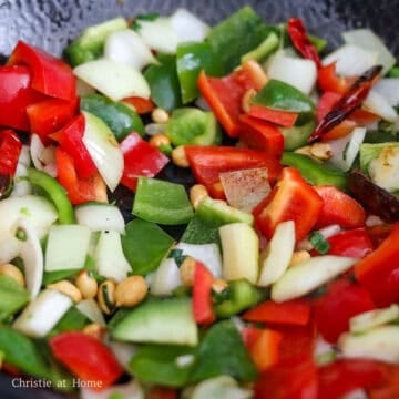 On medium-high heat, add more oil if the pan is dry. Stir-fry dried red chilies, peanuts, white onions, and green onions for 1 minute. Toss in bell peppers and stir fry for 1 minute.