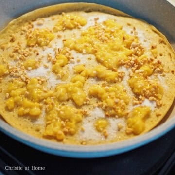 Once the bubbles have formed, evenly sprinkle a generous amount of sugar, creamed corn, crushed peanuts and small slices of butter across the pancake. 