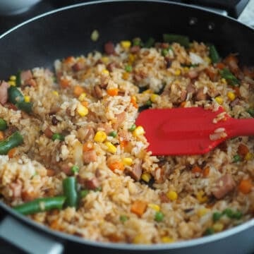Toss in cold day-old rice and break it up with a spatula. Season rice with soy sauce, ketchup and sesame oil. Toss until every rice granule is colored brown.