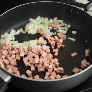 Heat vegetable oil in a large pan on medium-high heat and fry onions and diced spam until spam is slightly browned on the edges. 