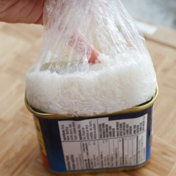 Cover the rice with the plastic wrap. Then using your fingers, pack the rice into base of can until top is flat. Be careful not to cut yourself along the sharp edges of the can, feel free to use a utensil to help you with this step. Remove the block of white rice from can by pulling the cling film out and unwrap it on a cutting board. 