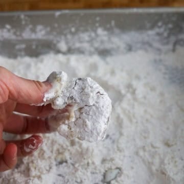 Shrimp being coated evenly in a seasoned cornstarch mixture in a shallow bowl.