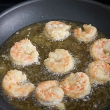 Shrimp frying in hot oil in a pan until golden brown on both sides.