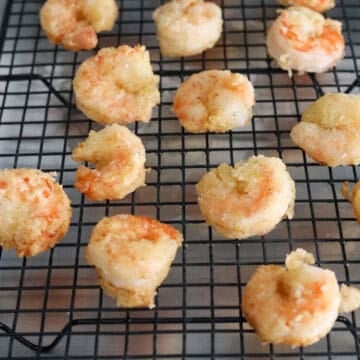 Fried shrimp resting on a wire rack or paper towel-lined plate to drain excess oil.