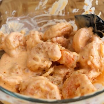 Crispy shrimp being tossed in a glossy sauce and garnished with chopped green onions.