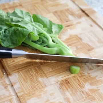 Chinese broccoli stalks with vertical slits at the base being washed under cold running water.