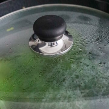 Steaming Chinese broccoli simmering under a closed lid.