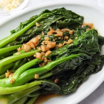 Glossy garlic Chinese broccoli arranged on a serving plate with savory brown sauce poured over top.
