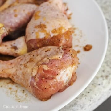 Raw chicken drumsticks soaking in a dark soy sauce and garlic marinade.