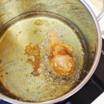 Chicken drumsticks frying in bubbling hot oil inside a deep pan.