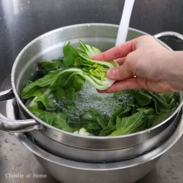 Slice baby bok choy into halves. Rinse the halved baby bok choy in cold water until it runs clear, and leaves are clean. Shake out as much excess water as possible. Set aside in the colander to continue straining. 