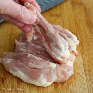 Raw bone-in chicken thighs lying skin-side down on a cutting board.