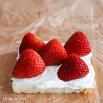 Lay out a large sheet of plastic wrap on a cutting board and place a slice of bread on top. Spread a thin layer of the whipped cream on top of the bread and then place the strawberries in an 'X' shape pointing in the same direction. Remember which direction they’re pointing in.