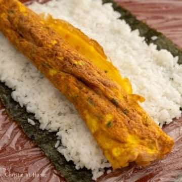 Place the rolled omelette in the center of the rice. Begin firmly rolling it away from you until you reach the end ensuring the seaweed border sticks to the rest of the kimbap. 