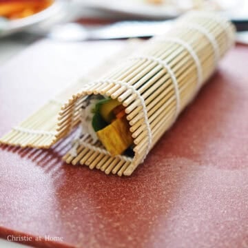 With the end closest to you, begin rolling the kimbap keeping the filling ingredients inside the roll, until you reach the very end. Let the roll sit on the empty border so the heat seals the flap onto the roll. 