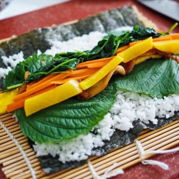Place two perilla leaves in the middle of the rice, followed by two strips of the cooked egg and one strip of pork belly. Use a knife and spread 1 tablespoon of ssamjang paste over your pork belly. Then layer with sautéed carrots, spinach and a strip of pickled daikon.