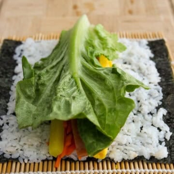 In the middle of the rice, neatly place an equal portion of cooked carrots, a strip of pickled daikon, a strip of egg, two strips of spam into a pile and a folded piece of lettuce on top of everything.